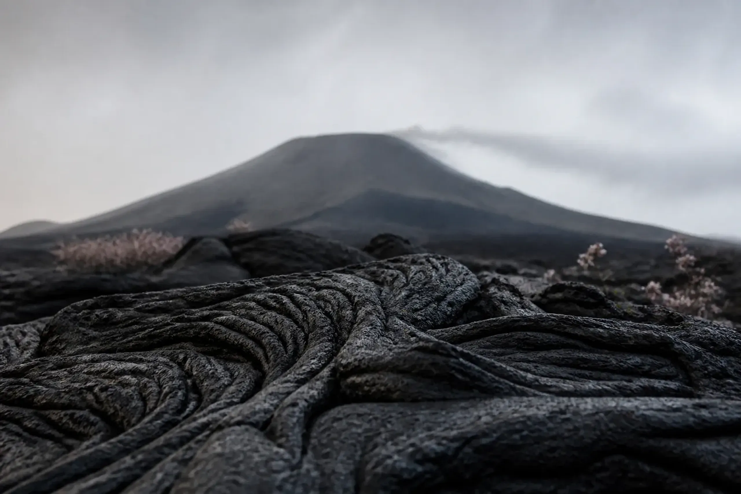 Hardened black lava fields on Sakurajima volcano with a faint ash plume above the peak