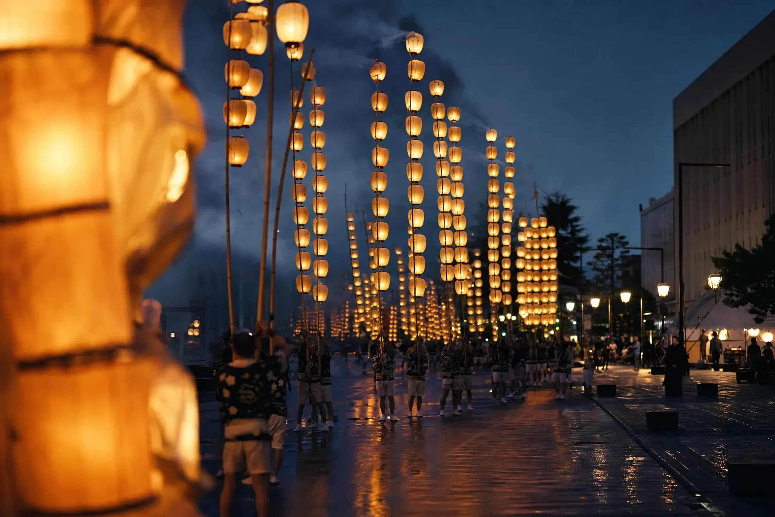 Rows of 46-lantern Ōwaka Kantō poles resting upright with real candles glowing after a night procession in central Akita City