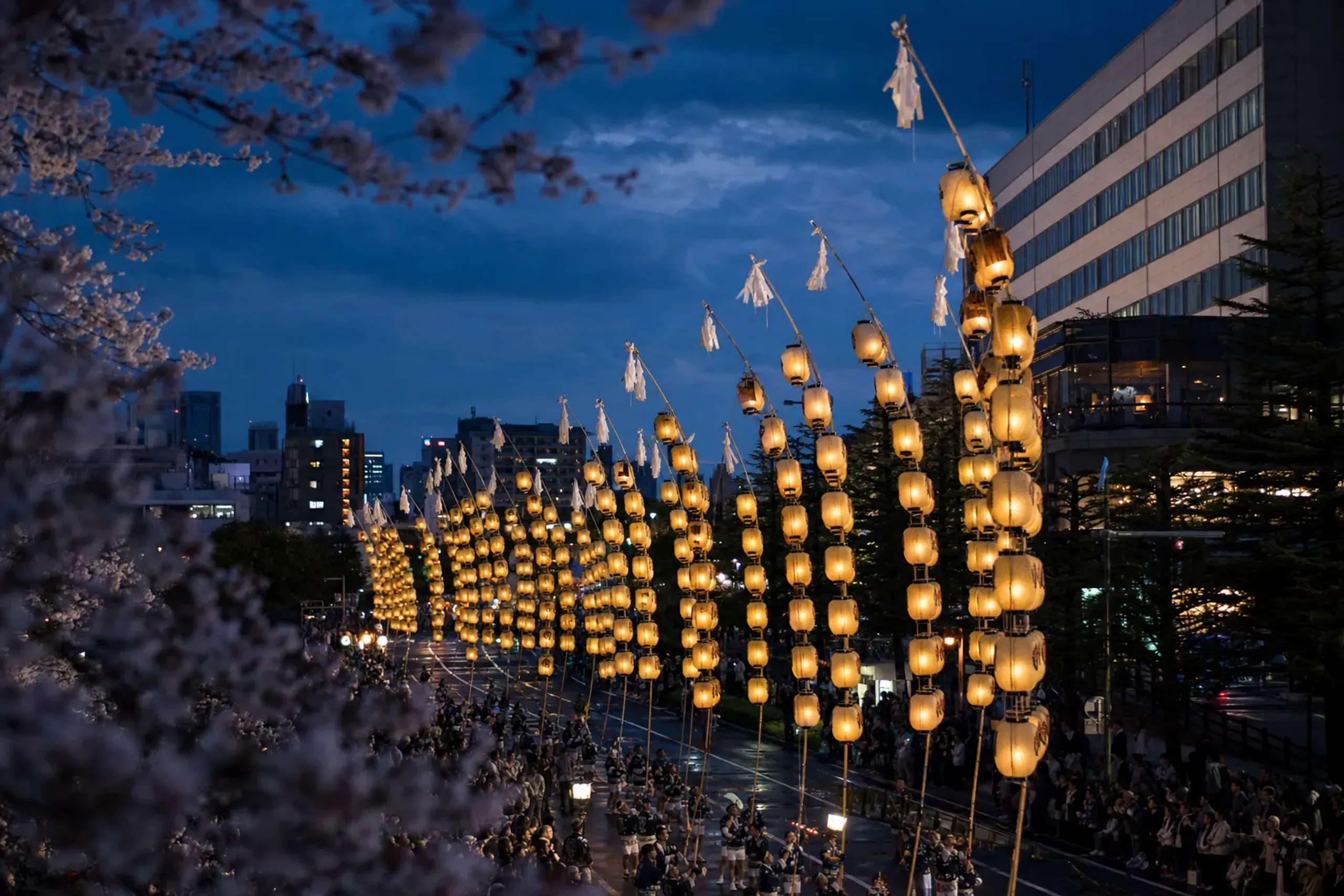 Dozens of illuminated rice-ear Kantō lantern poles rising in unison against the night sky over Kantō Ōdori in Akita City