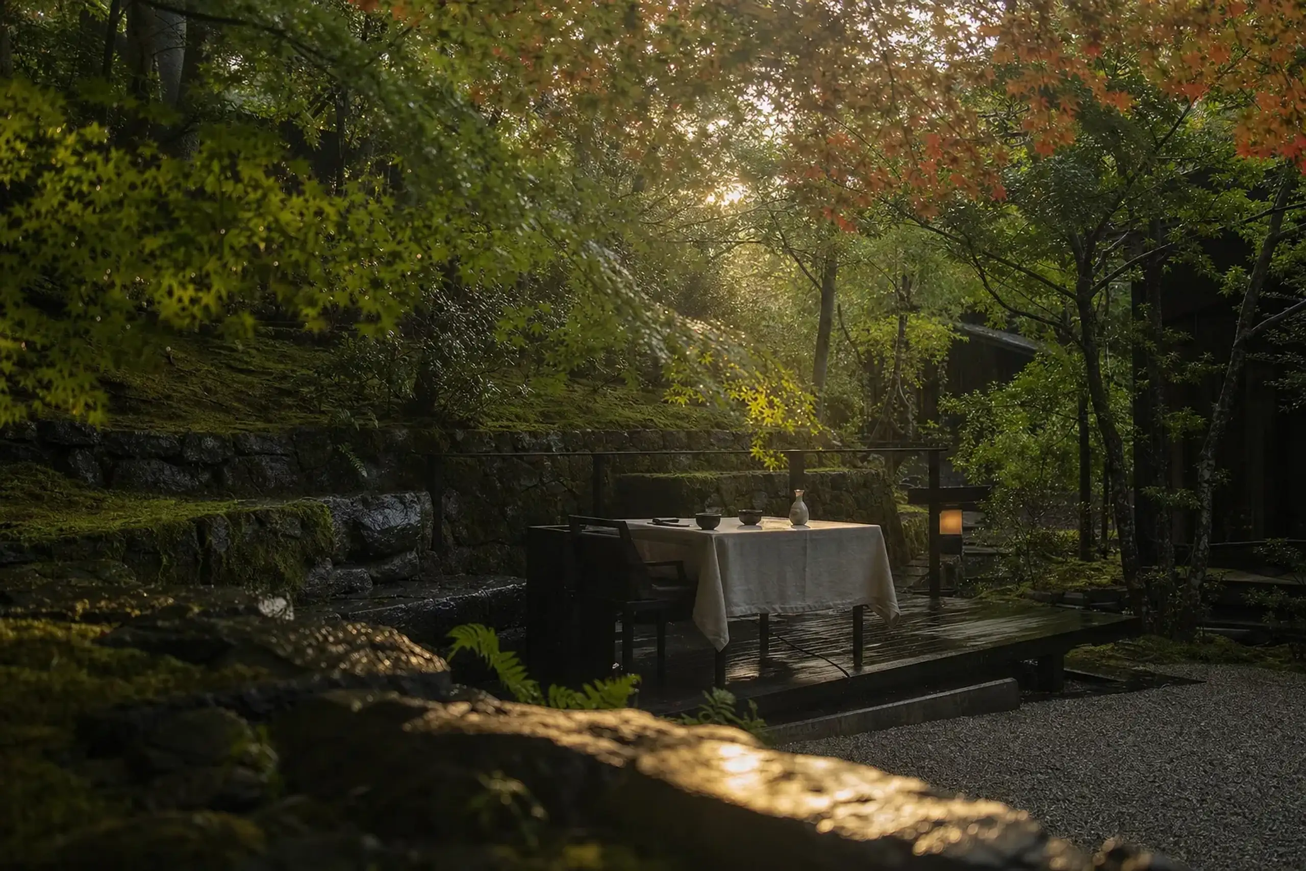 A vivid autumn maple foliage canopy over the forested terraces of Aman Kyoto during foliage season, framing an open-air garden dining setting