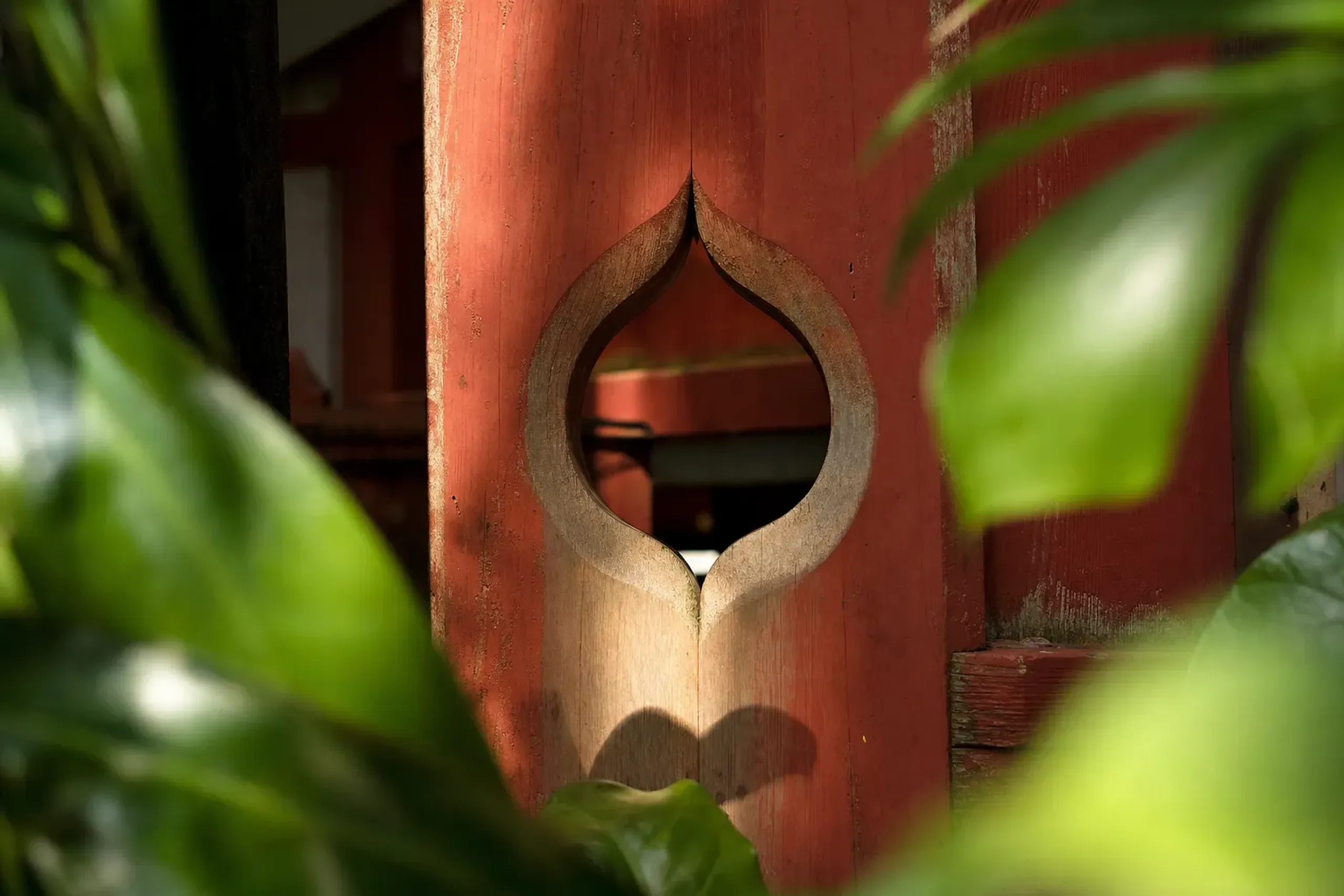 heart-shaped inome motif carved into the wooden architectural details of Aoshima Shrine, framed by subtropical foliage