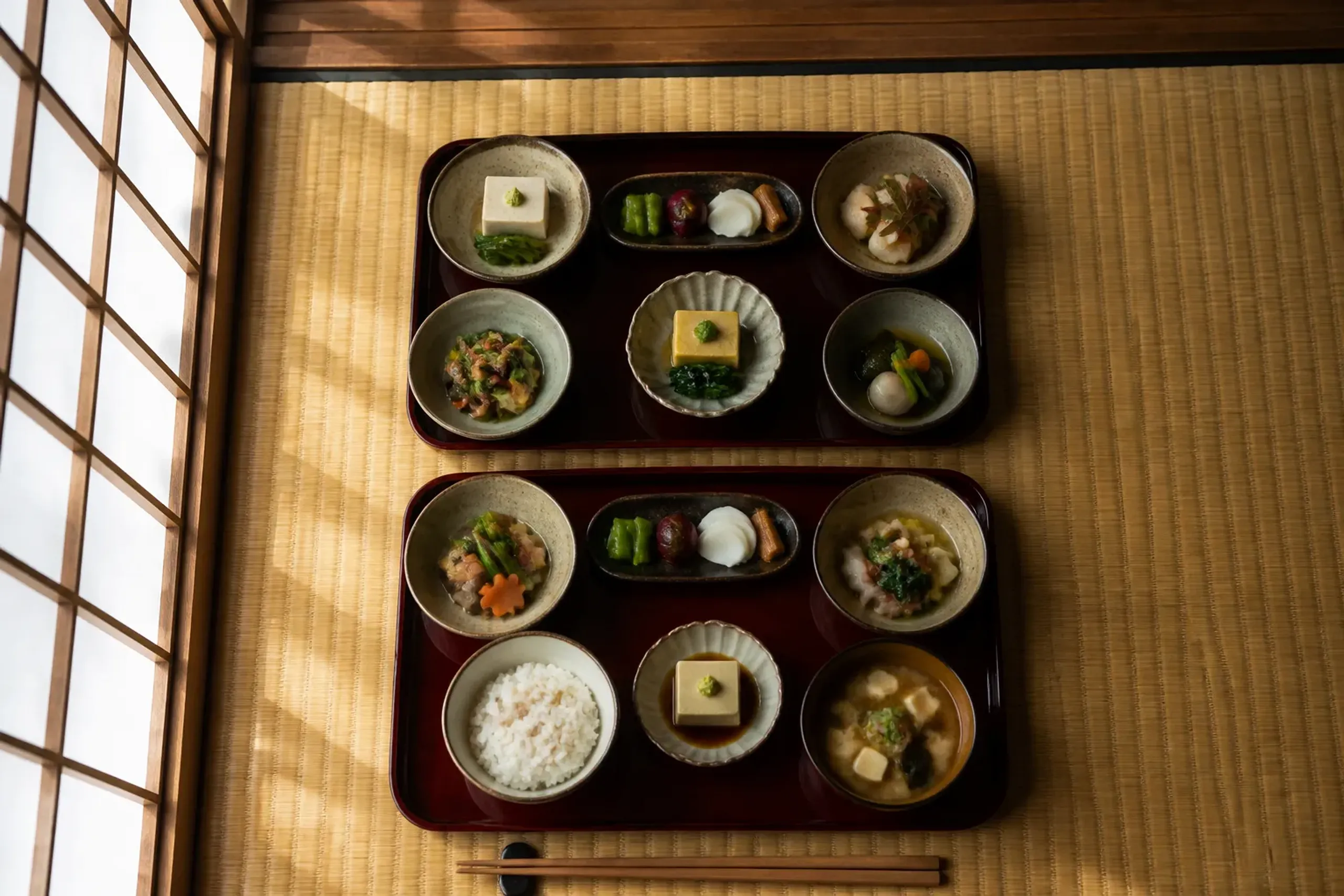 An overhead, table-level still life of a shojin ryori set meal served in a quiet temple dining room: lacquer trays on tatami with multiple small ceramic bowls of seasonal vegetable dishes, rice, miso