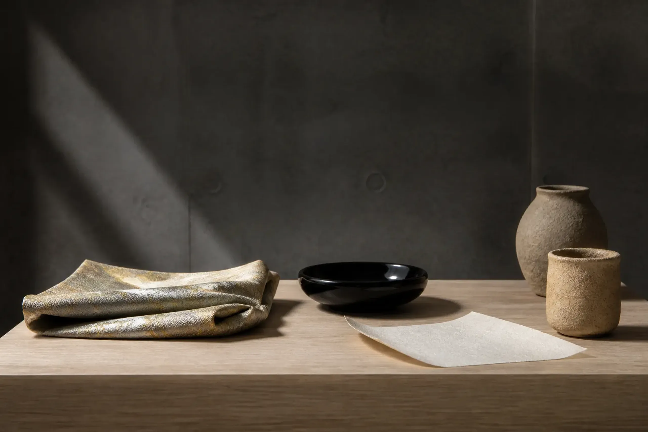 a close-up arrangement of Nishijin silk textiles, lacquerware, handmade paper, and unglazed clay vessels displayed together under soft directional gallery lighting, showing the traditional Kyoto craft