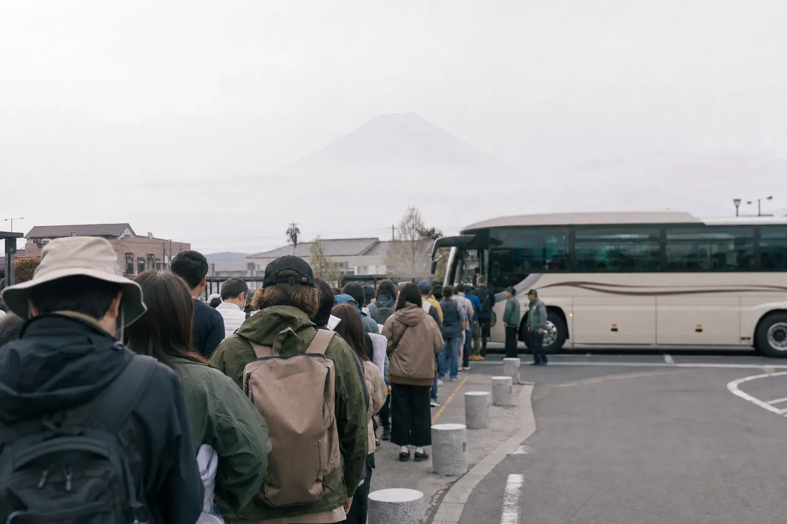 A shuttle bus queue at Kawaguchiko Station with visitors boarding festival transfer buses, Mount Fuji faint in the background