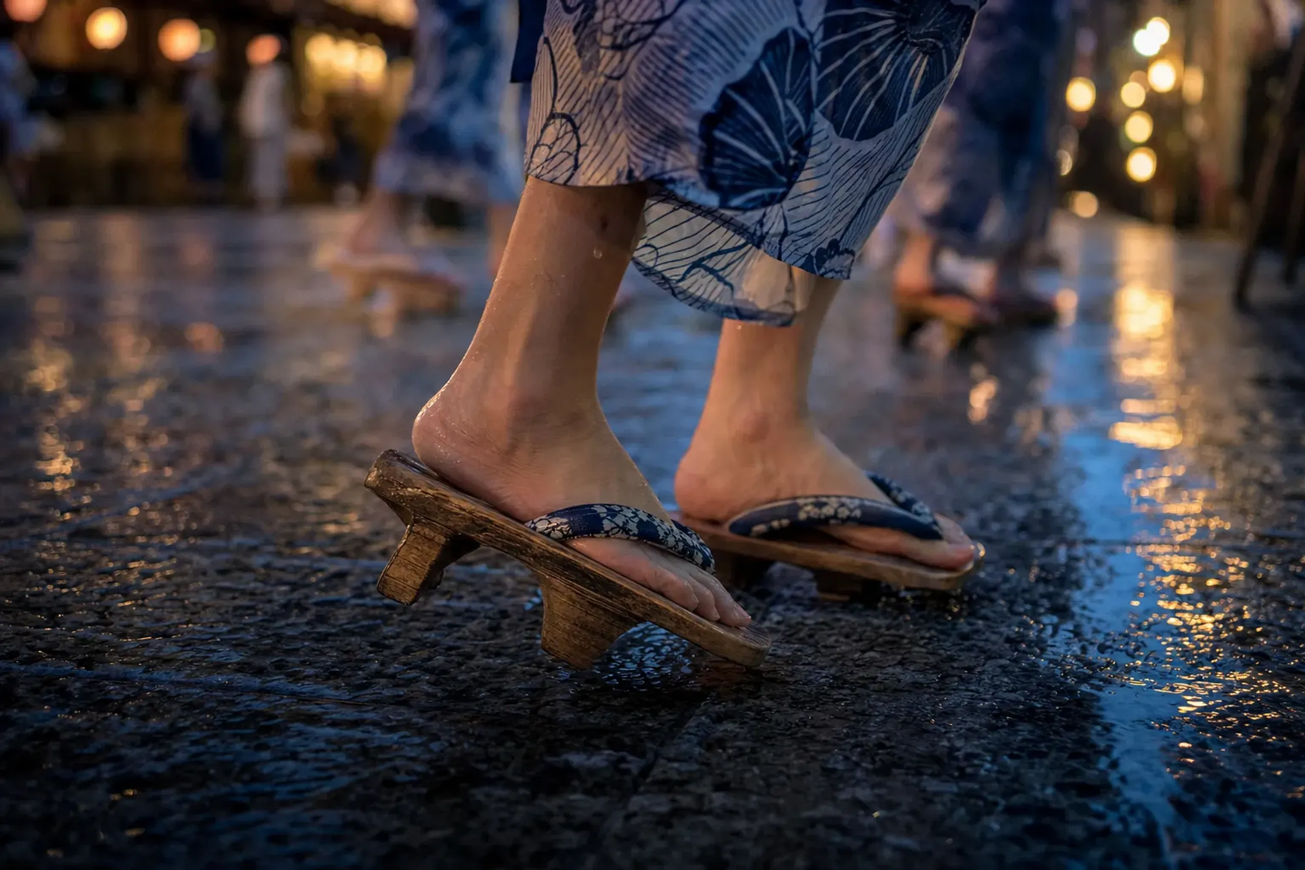 Wooden geta sandals mid-step on worn stone paving, captured in the lamplight of the night dance