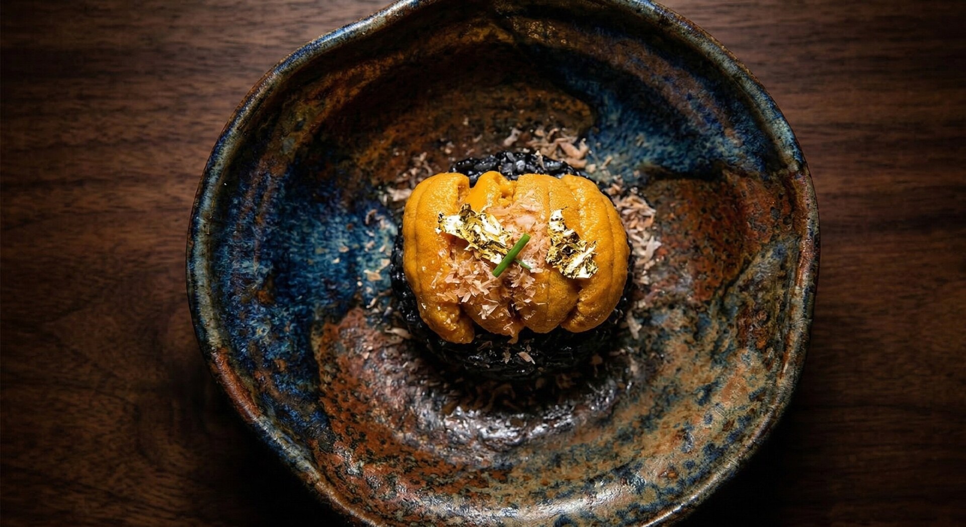 Exquisitely plated high-end kaiseki dish featuring fresh sea urchin and edible gold leaf on artisan ceramic ware, set under dramatic lighting to highlight Hakodate's luxury gastronomy.
