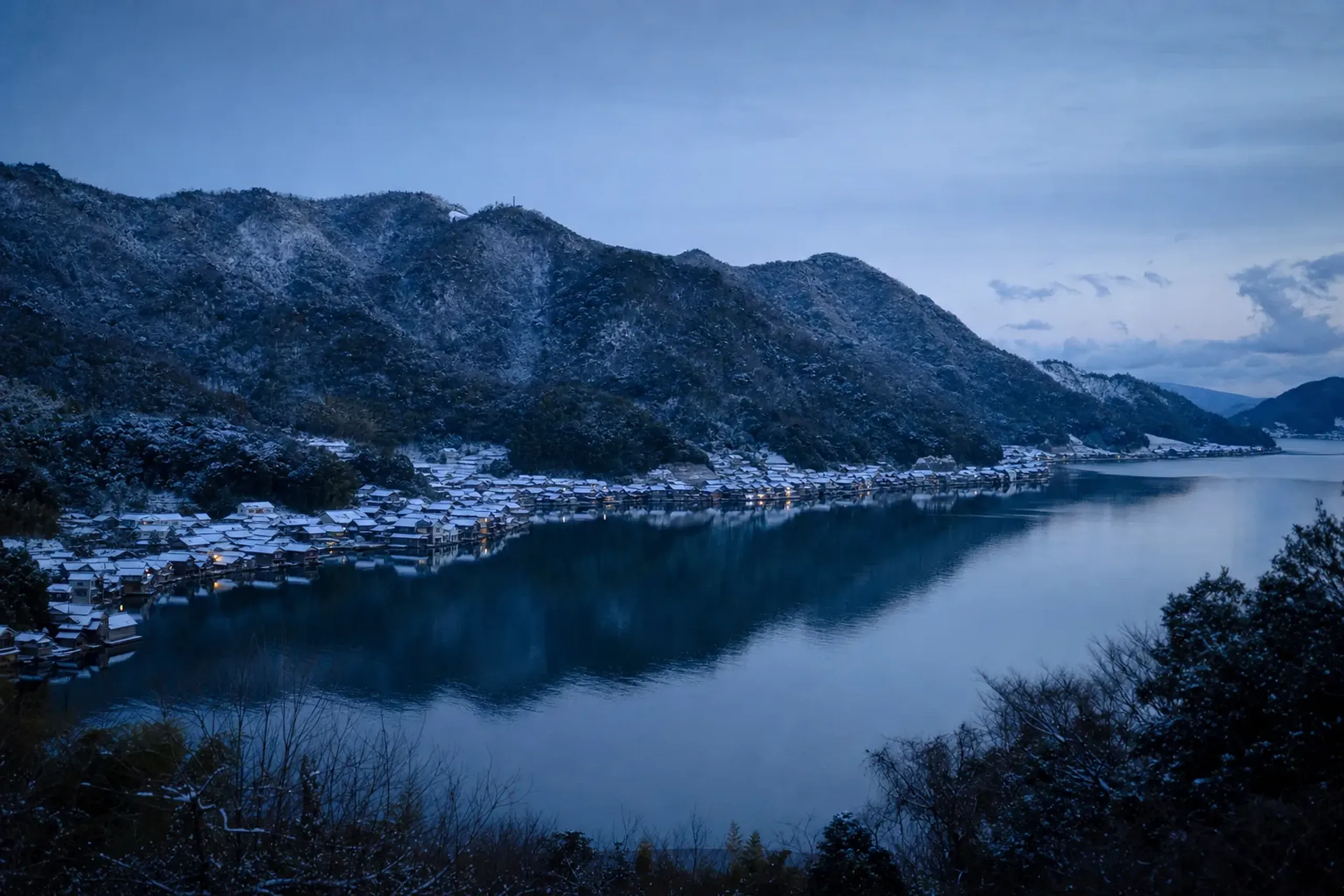 The full five-kilometre curve of Ine Bay at dusk with rows of funaya reflected in the mirror-still water beneath the surrounding mountains