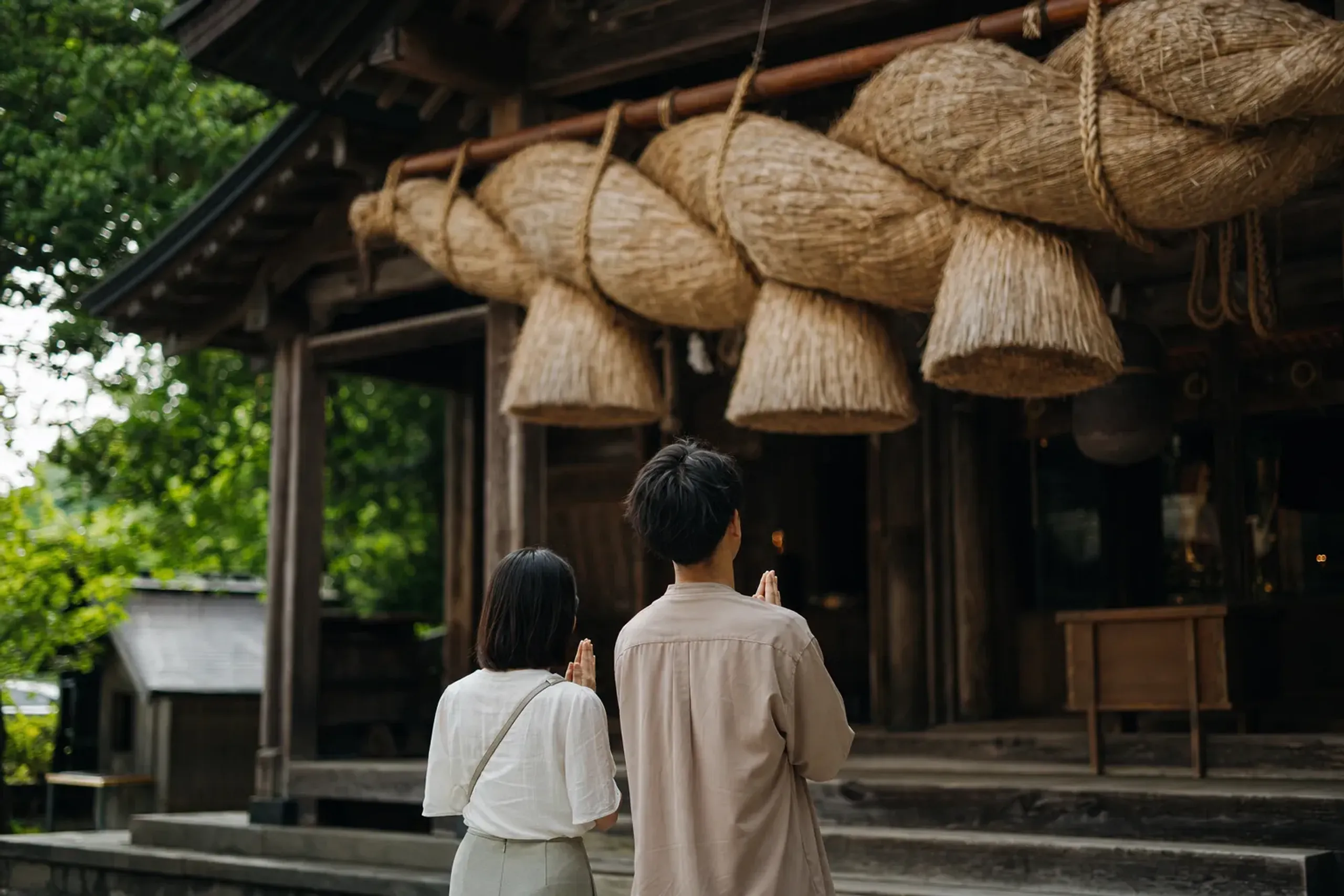 The offering hall of Izumo Taisha with worshippers' hands raised in prayer before its thick straw shimenawa rope