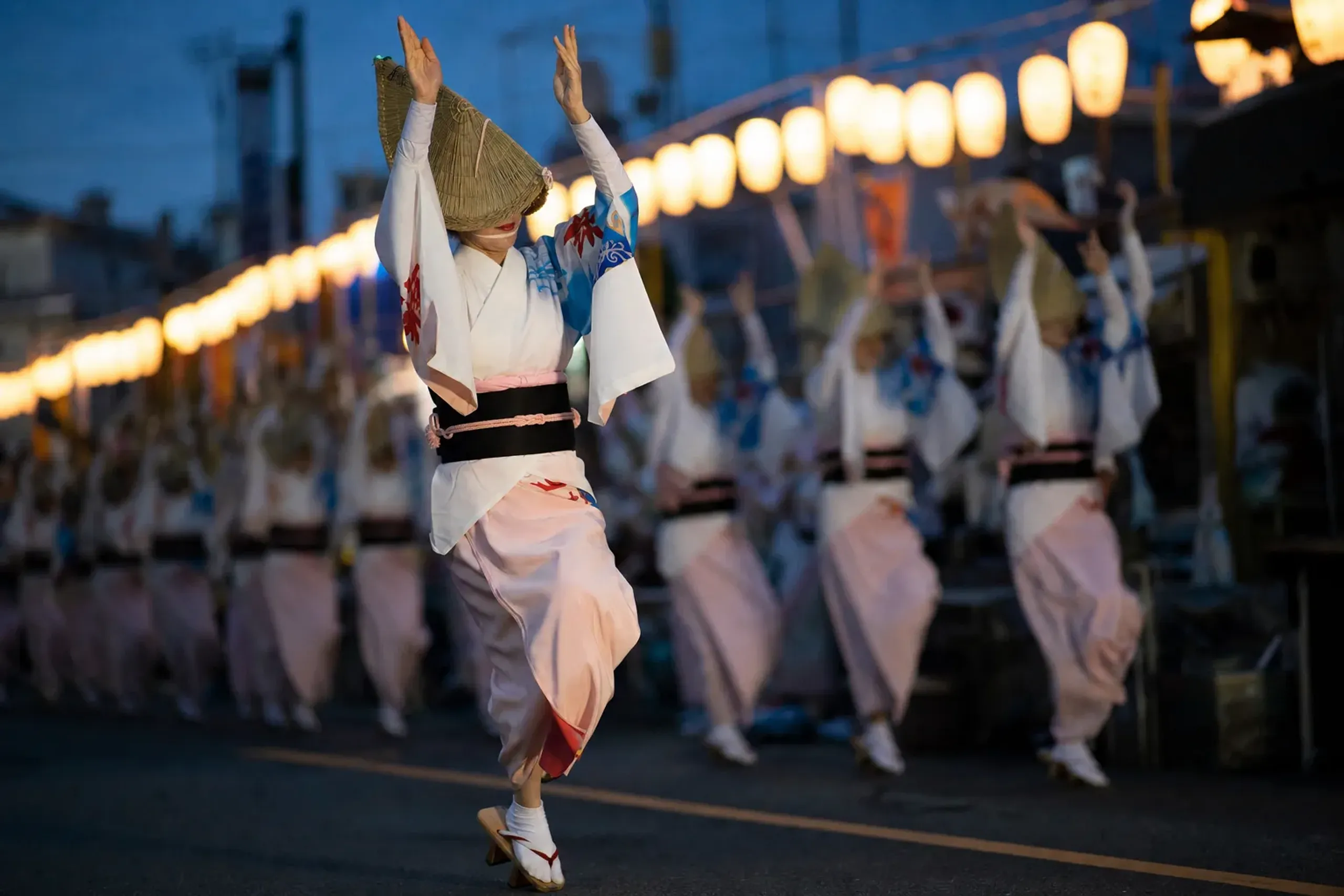Awa Odori dancers in Tokushima performing the traditional ren group dance at night, with paper lanterns and wooden geta sandals, under the summer evening sky