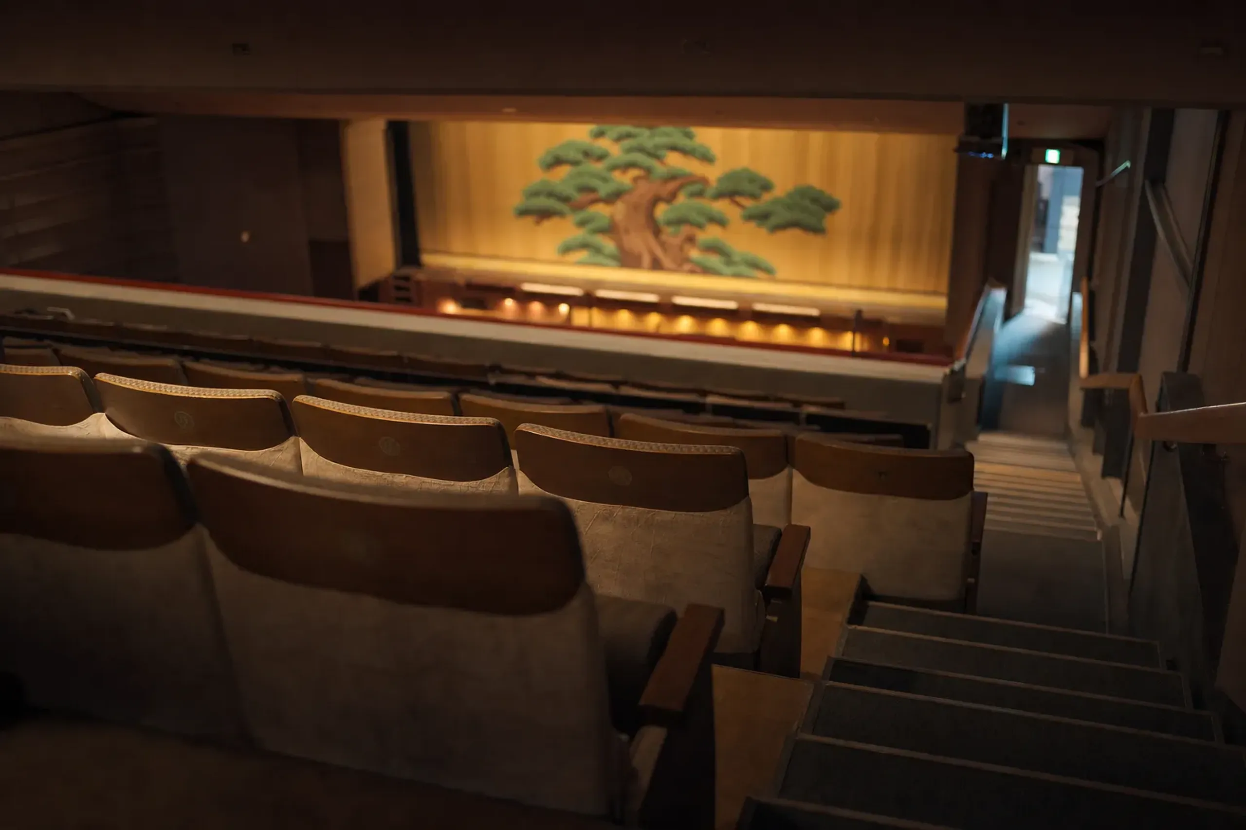 The 4th-floor unassigned single-act seating rows of Kabuki-za viewed from the back, with an aisle exit leading toward Ginza