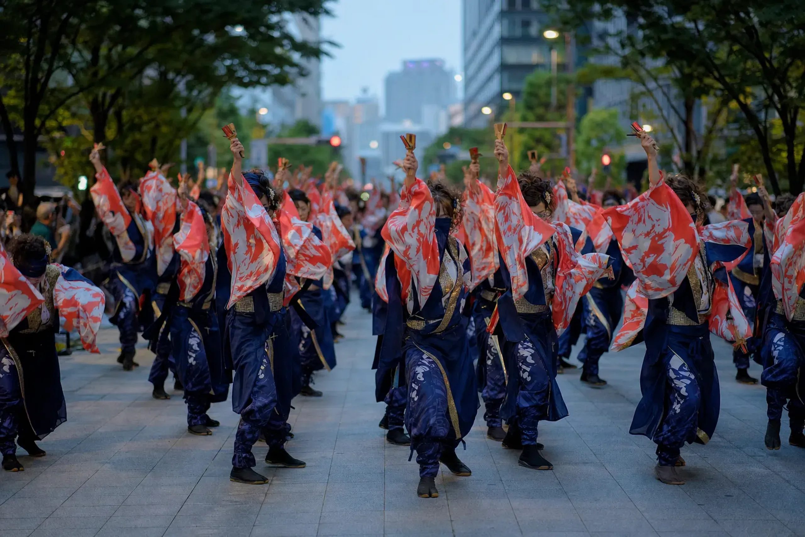 A line of Yosakoi dancers in bright silk costumes advancing forward down Otesuji, naruko raised mid-clap