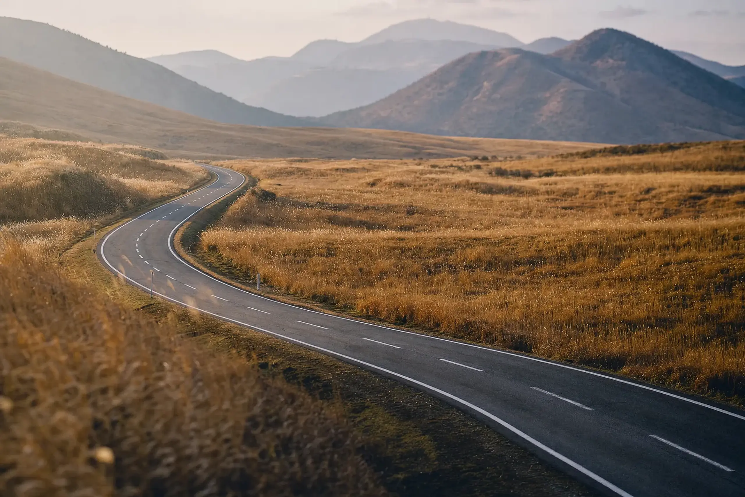 A winding mountain road crossing the remote Kuju Plateau within Aso-Kuju National Park, open volcanic grassland with no rail infrastructure in sight