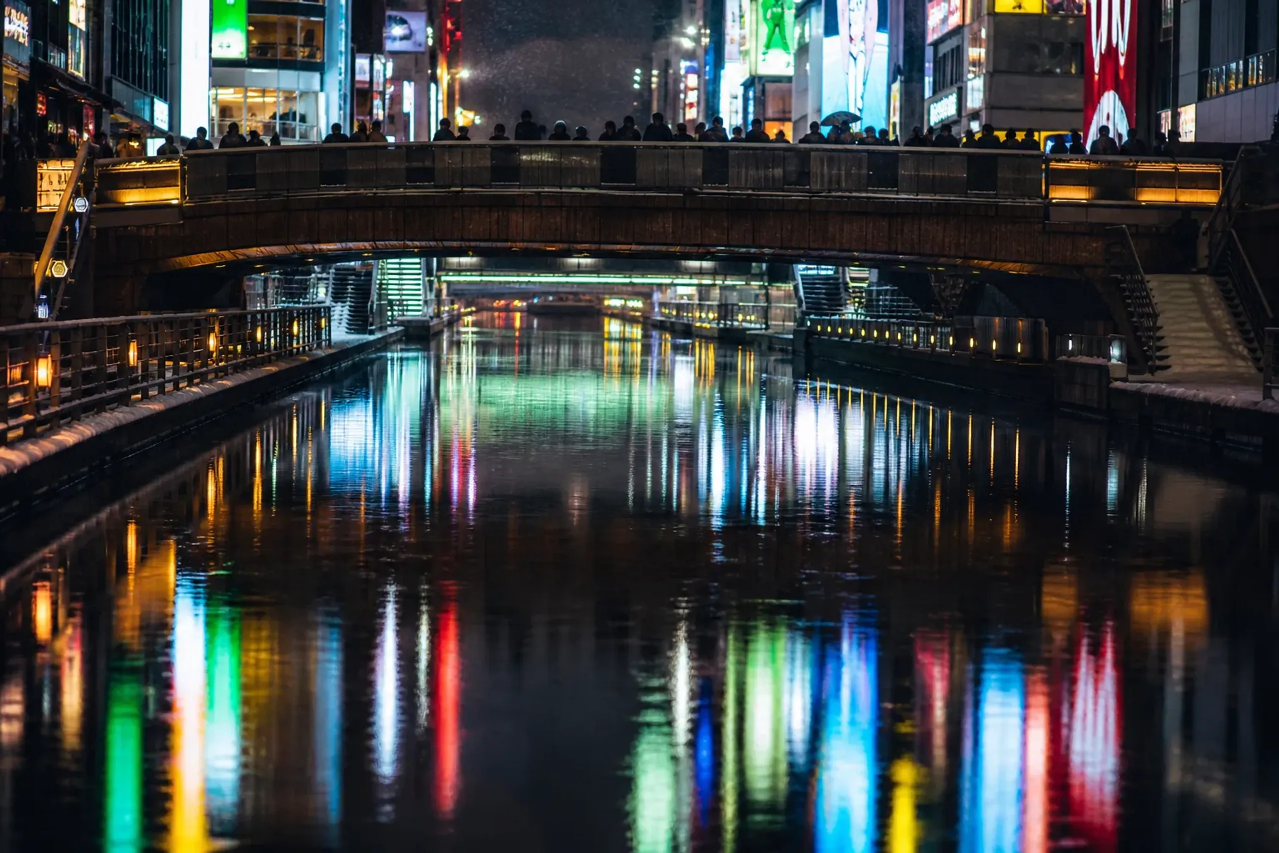 The neon-lit Dotonbori canal in Osaka at night, with the glowing signs reflecting on the water and the Ebisu Bridge crossing overhead