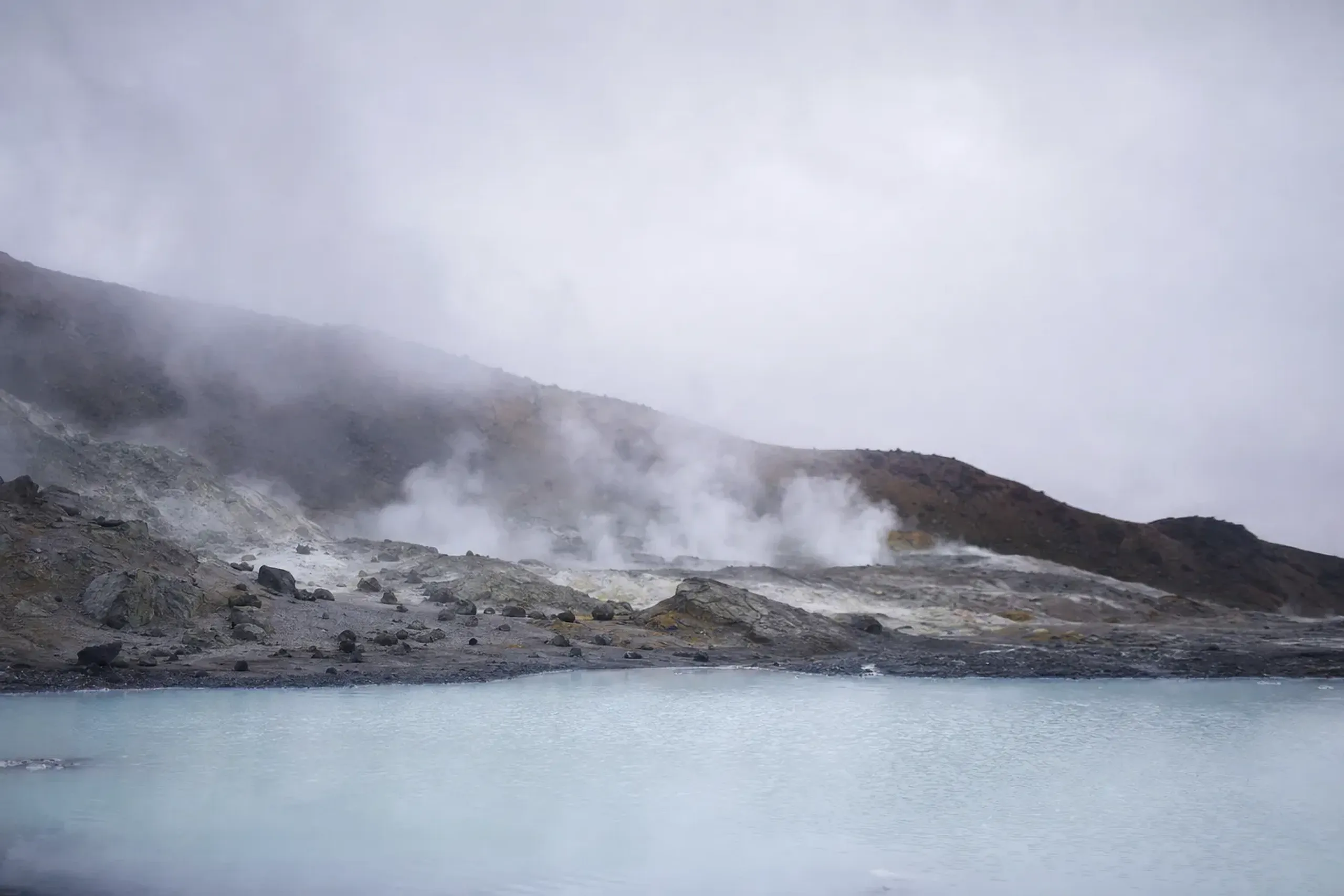 Pale lake and dark volcanic rock with rising steam at Osorezan in Aomori