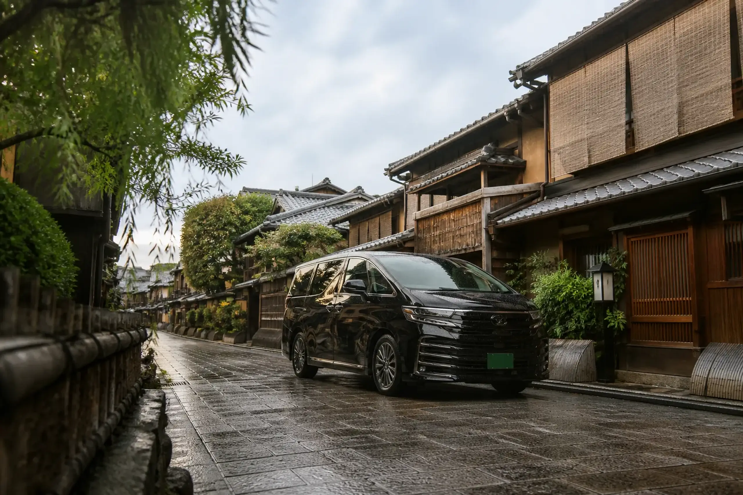 A black Lexus LM 500 with green commercial license plates parked and waiting on a narrow stone-paved lane in Gion, Kyoto, beside traditional wooden machiya townhouses