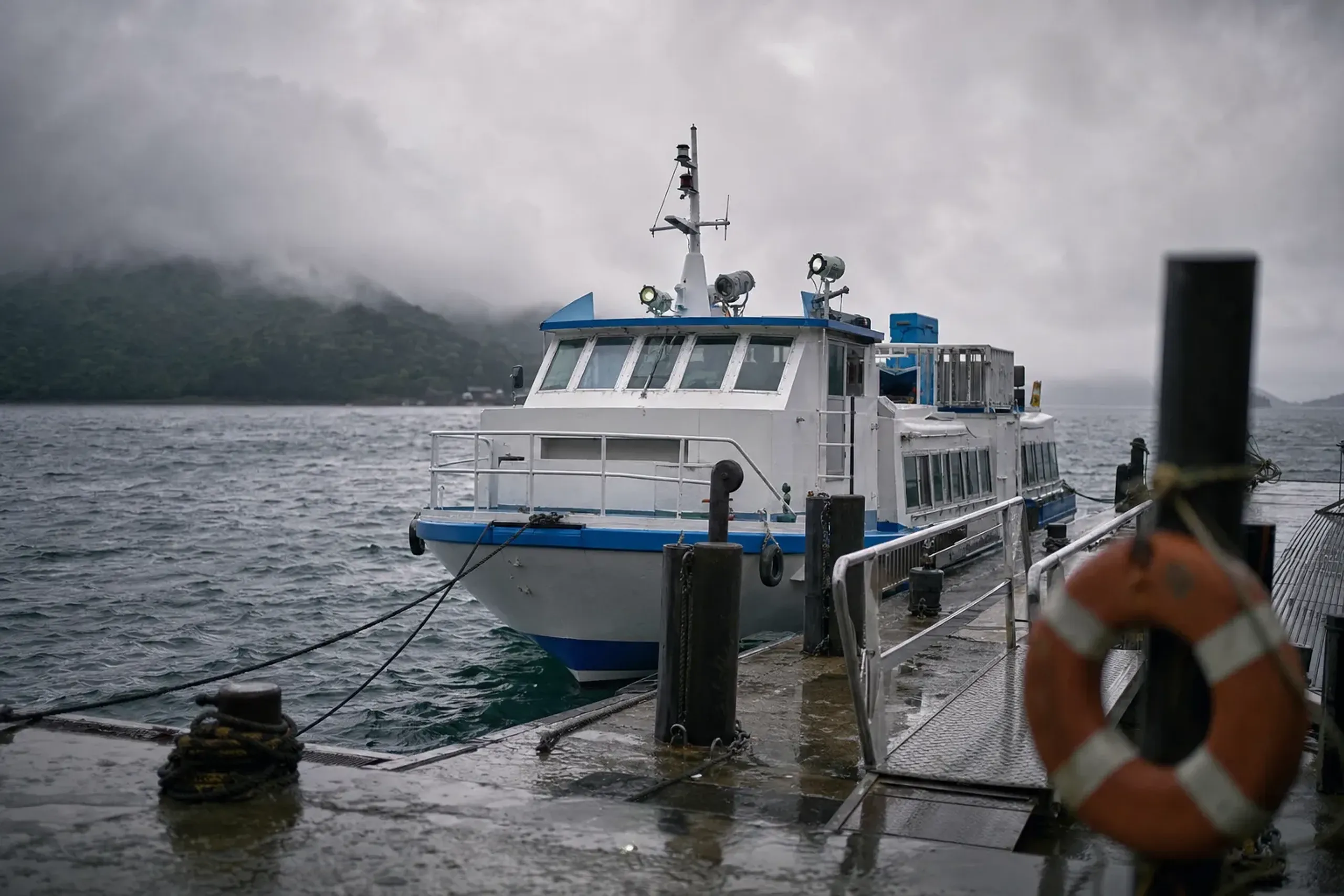 A small inter-island ferry moored at a Japanese coastal pier under heavy gray typhoon-season clouds with choppy seas