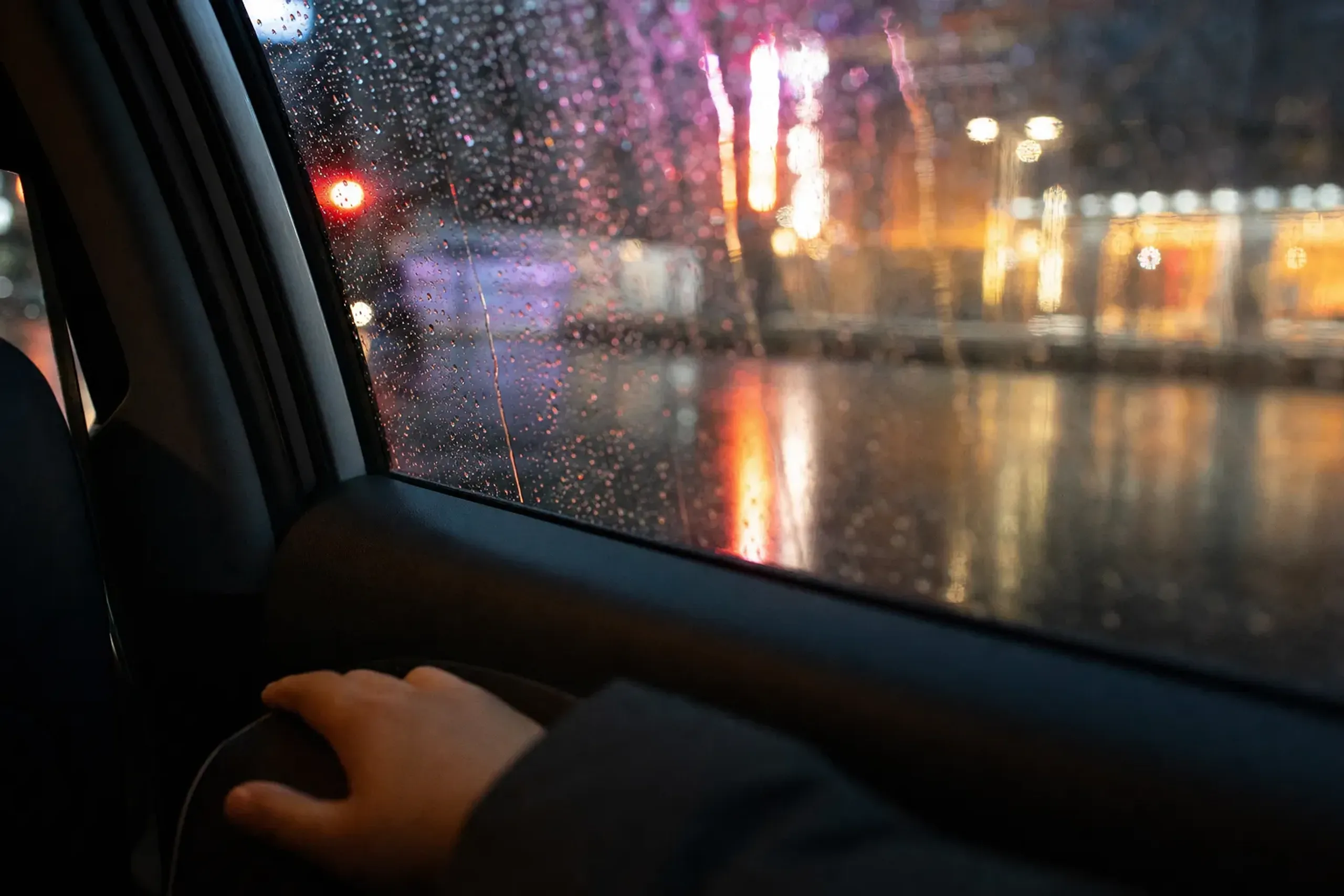 The sleek interior of a private luxury sedan with rain streaking the windows and reflected neon on the wet street outside