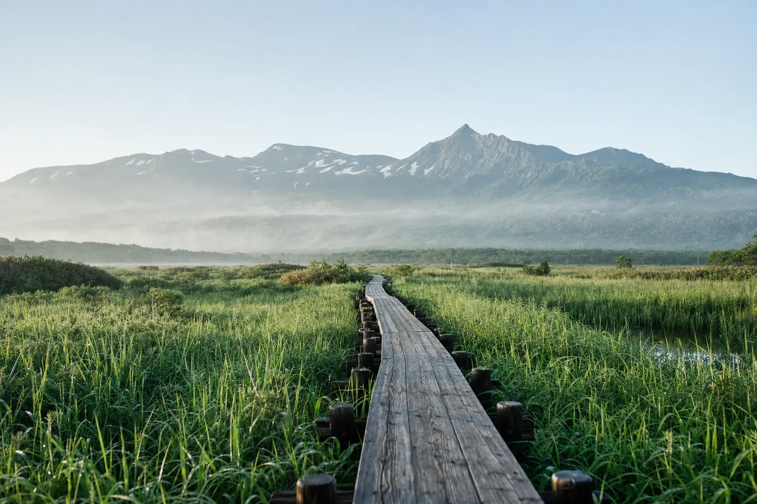 Wooden boardwalk at Shiretoko Five Lakes surrounded by lush green vegetation and mountains
