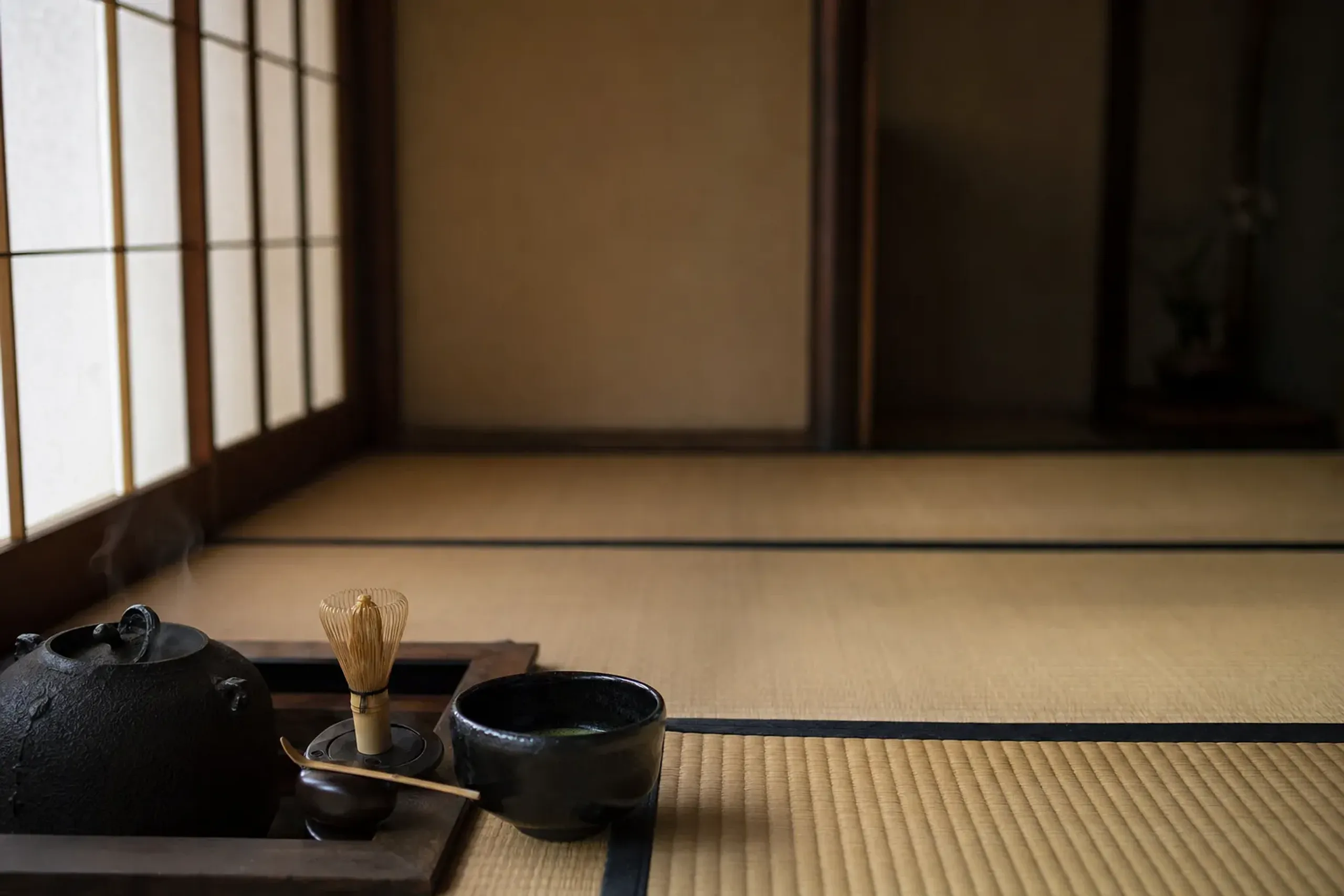 an Urasenke-style tea setting with a black raku chawan, bamboo whisk, and iron kettle on tatami