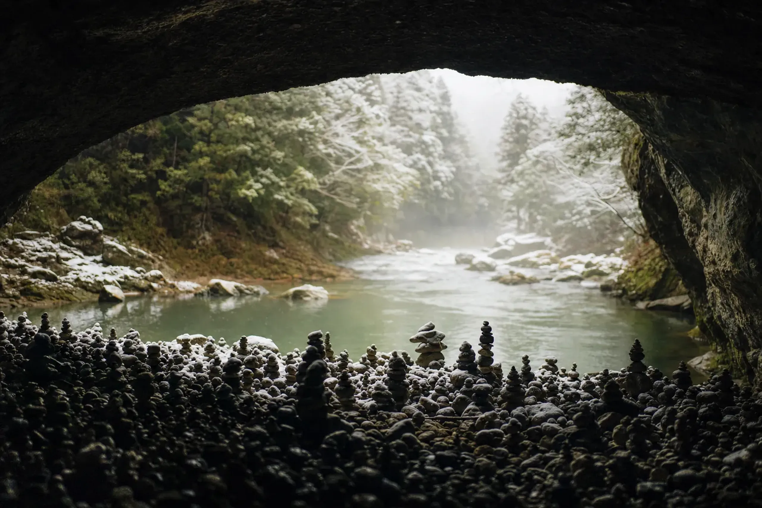 the wide mouth of Amano-Yasukawara cave with countless small stacked wish-stones arranged across its floor near the Iwato River