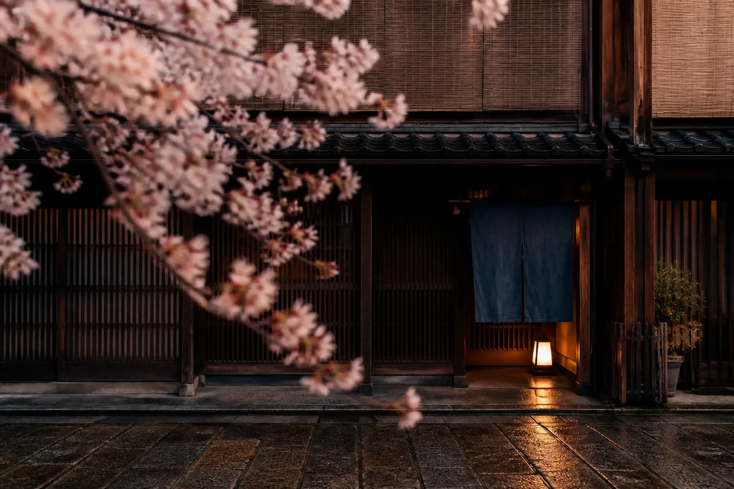 Traditional Japanese doorway with noren curtain and lantern light on a rainy stone street at night