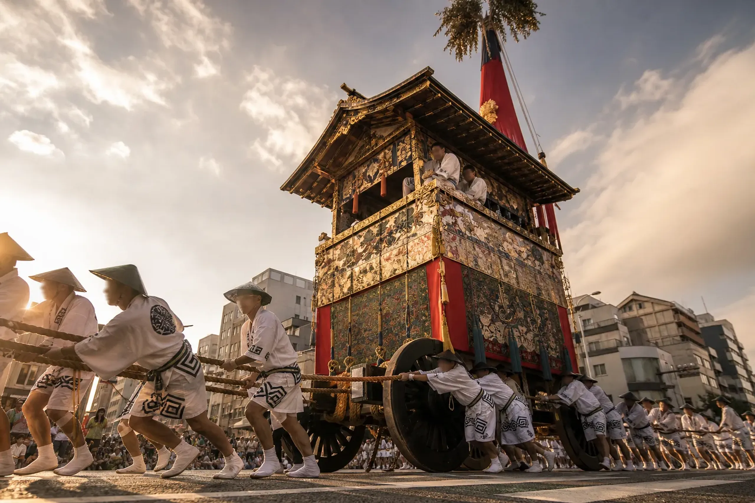 A towering Yamaboko float of the Gion Matsuri procession in Kyoto, decorated with ornate tapestries and lantern tiers, moving along Shijo Street in July