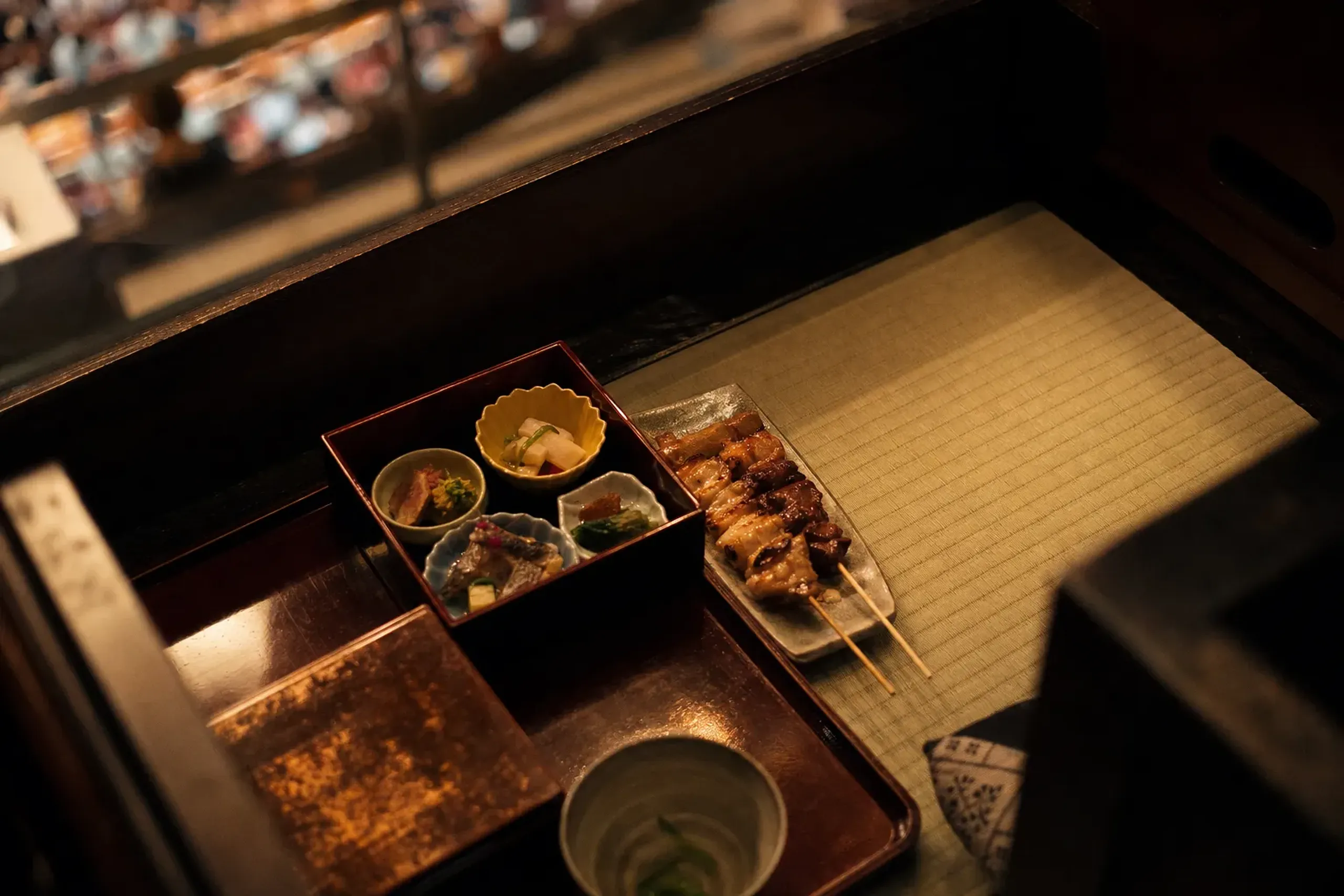 A teahouse bento box and skewers of yakitori arranged on a masu-seki tatami box seat