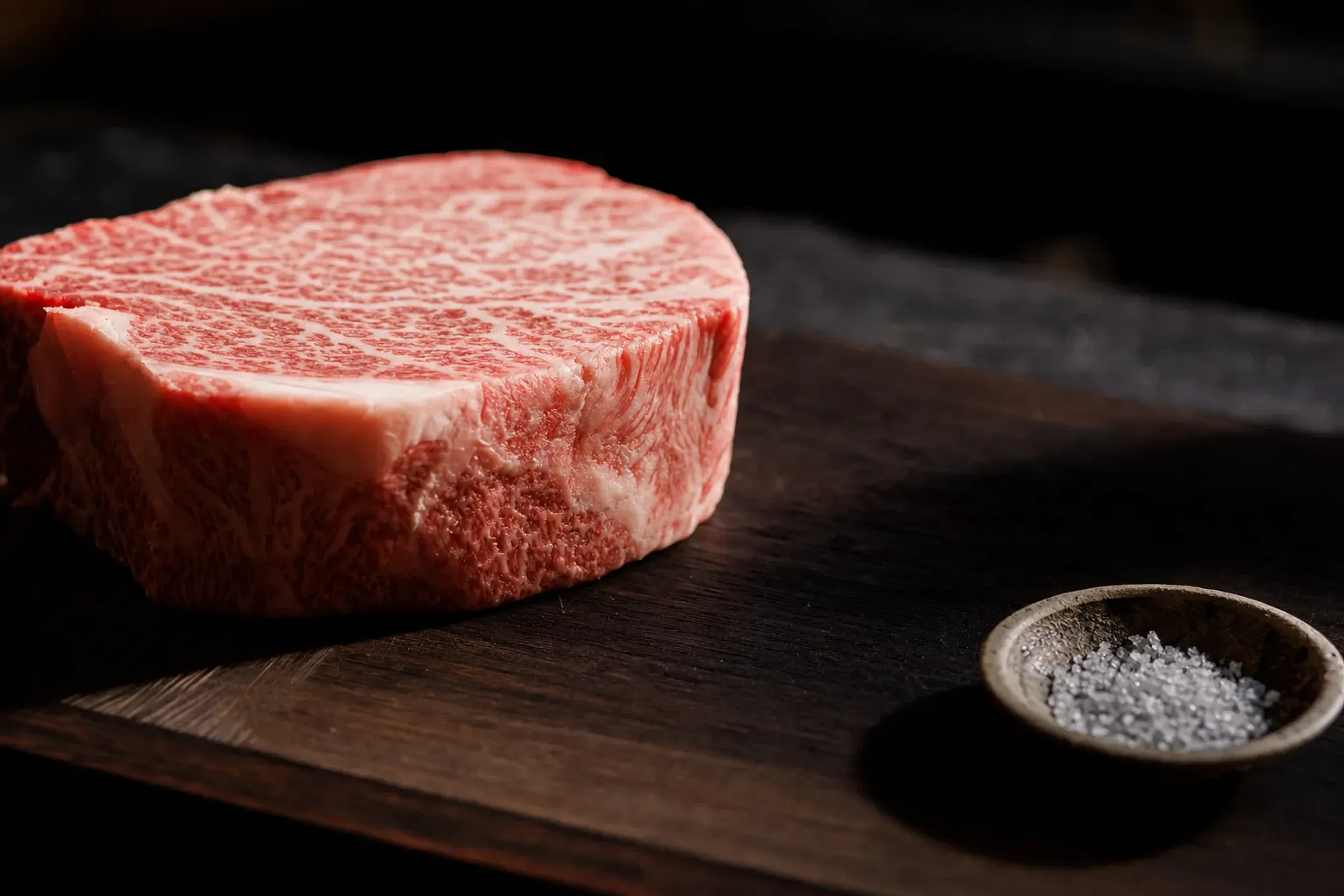 thick plush Matsusaka wagyu fillet with heavy white fat webbing, resting beside a small dish of coarse salt