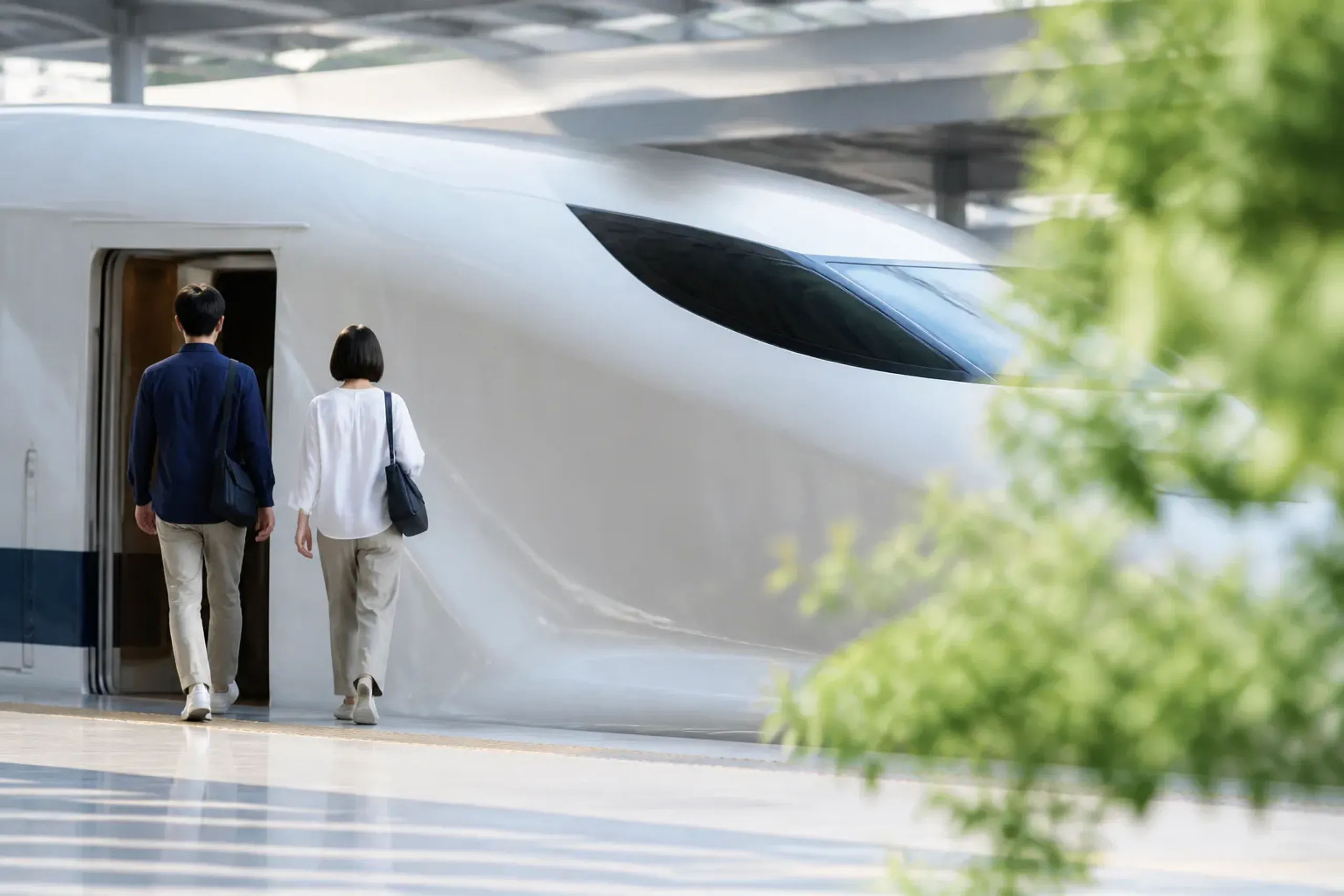 Travelers with small carry bags on a Shinkansen platform with a train behind them