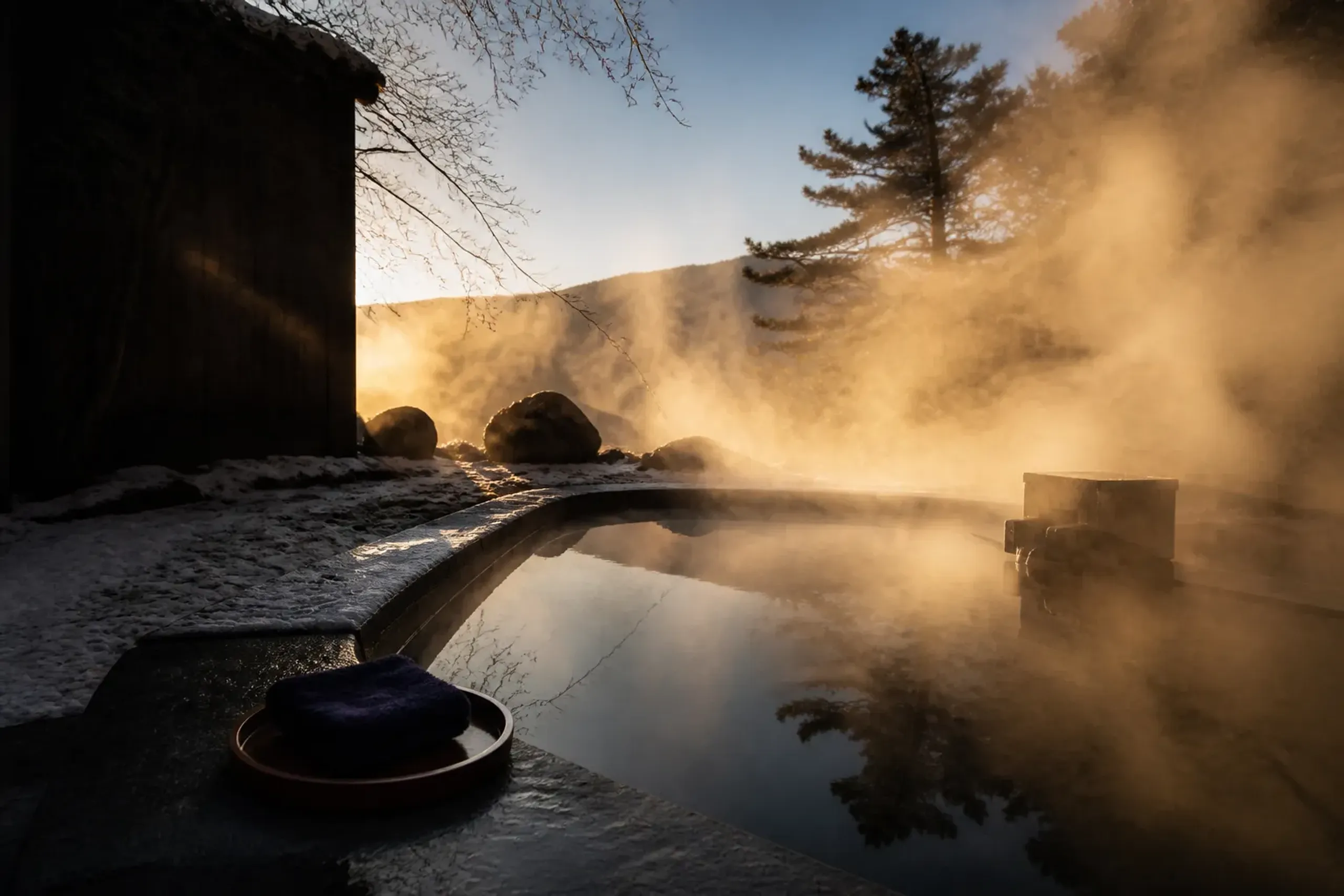 Steaming outdoor onsen bath in winter with snow on stone edges near Tokyo