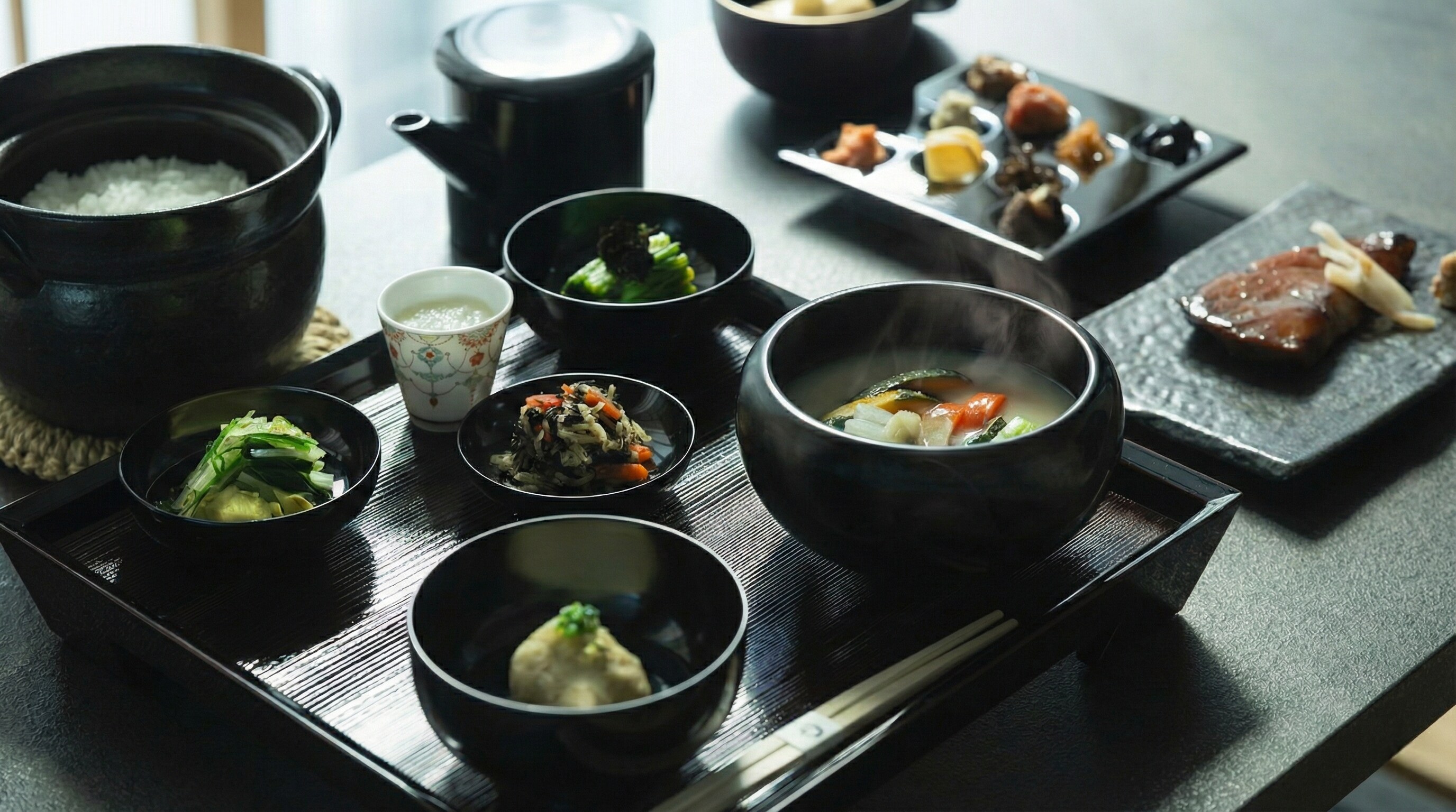 Traditional Japanese meal set, black lacquer tray, grilled fish, clay pot rice, vegetable soup, side dishes.
