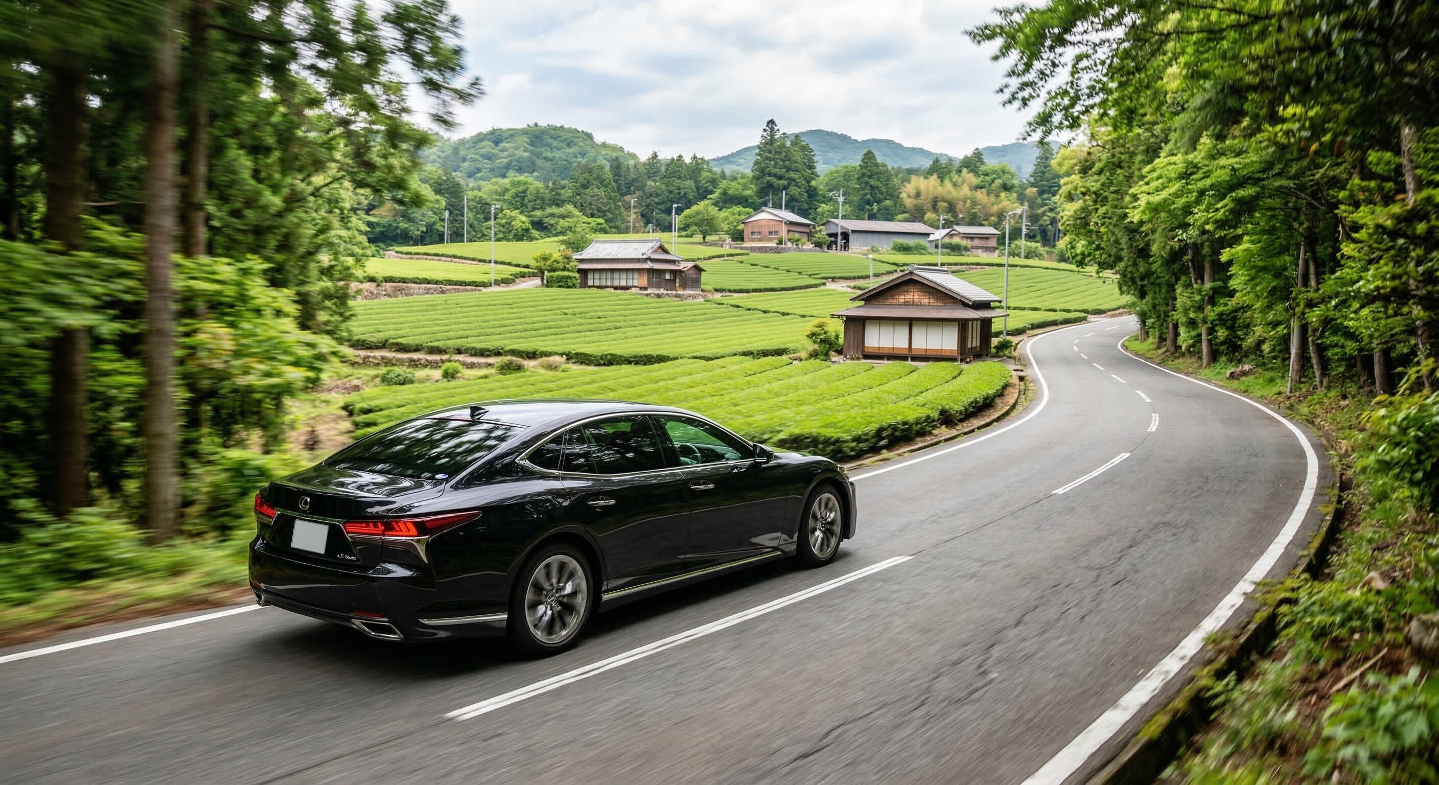 A sleek black luxury car driving along a peaceful, tree-lined road in the countryside of Uji, Japan.