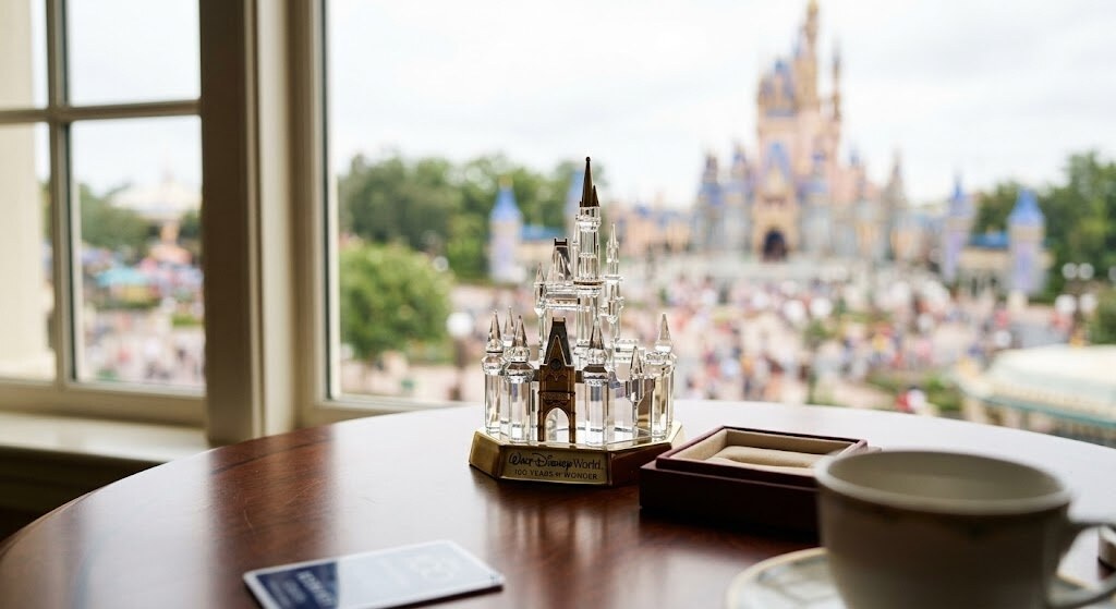Crystal Cinderella Castle souvenir on a wooden table by a window, with the theme park blurred in the background.