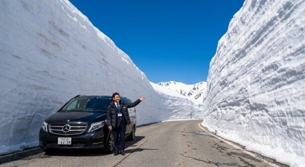 A clear view of the 20-meter-high Tateyama Snow Wall under a blue sky, featuring a luxury private vehicle and guide, representing an exclusive tour.