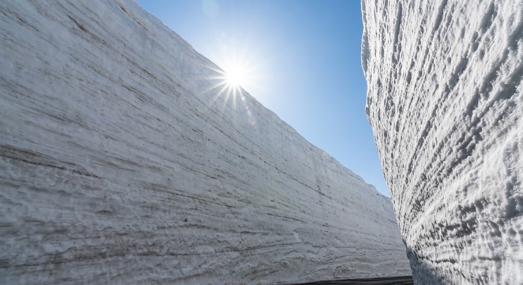 Bright sun between tall white snow walls, creating a narrow icy canyon.