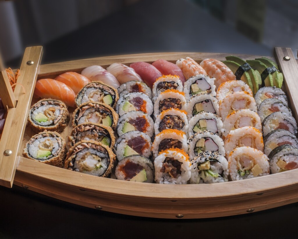 Sushi assortment in a wooden boat: nigiri and an array of maki rolls with avocado, cucumber, and fish fillings.
