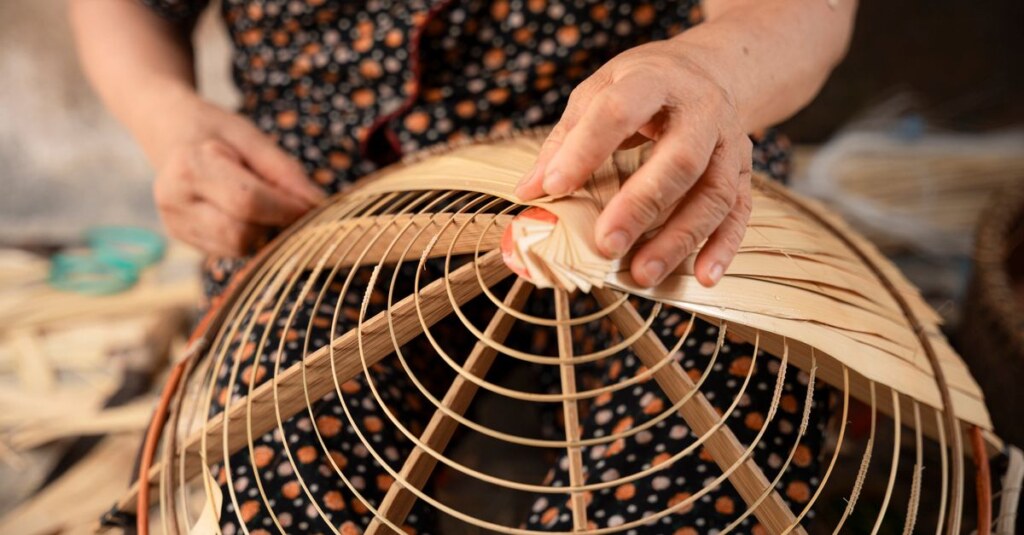 Close-up of an elderly person's hands weaving a bamboo basket frame