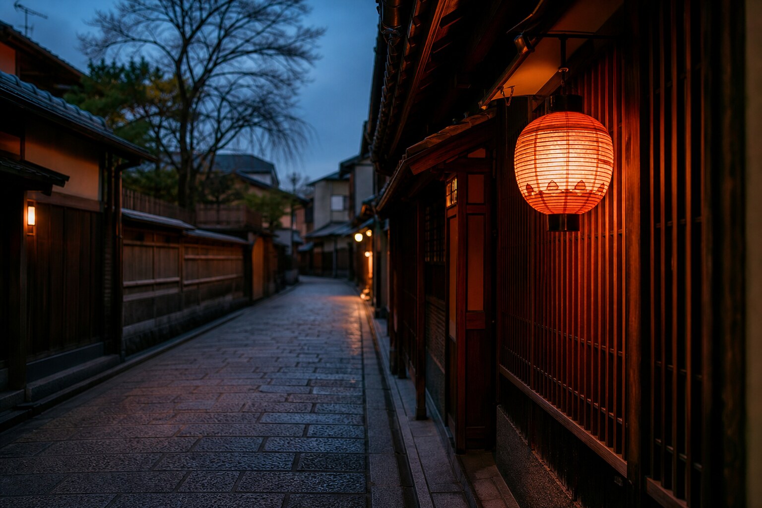 An empty stone street in Kyoto's Gion district lit by a traditional lantern at dusk.