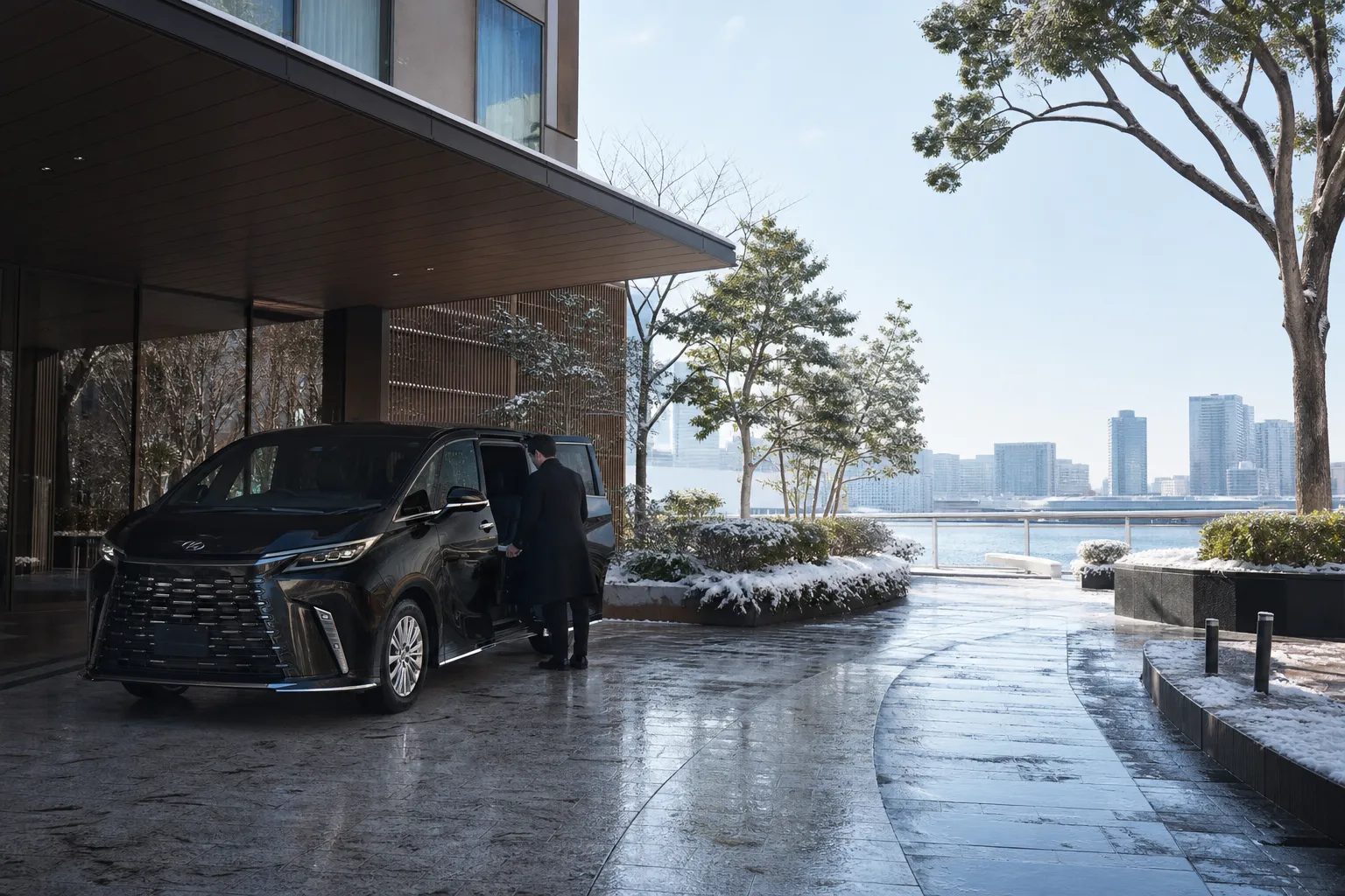 Black Lexus LM 500 luxury minivan with chauffeur at a Tokyo Bay hotel entrance at dusk
