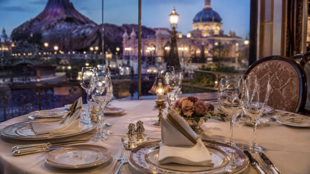 A luxurious, elegantly set table inside a premium Tokyo Disney Resort restaurant, overlooking a beautifully lit, exclusive themed backdrop.