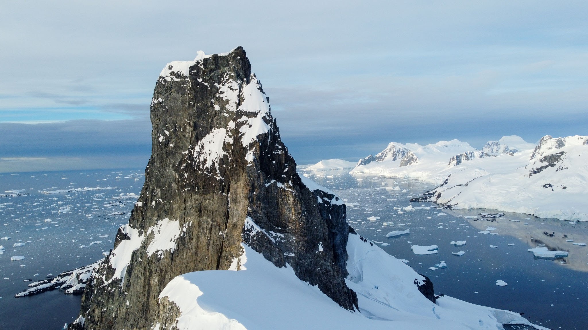 Majestic jagged rocky mountains covered in thick snow and ice under a blue Antarctic sky.