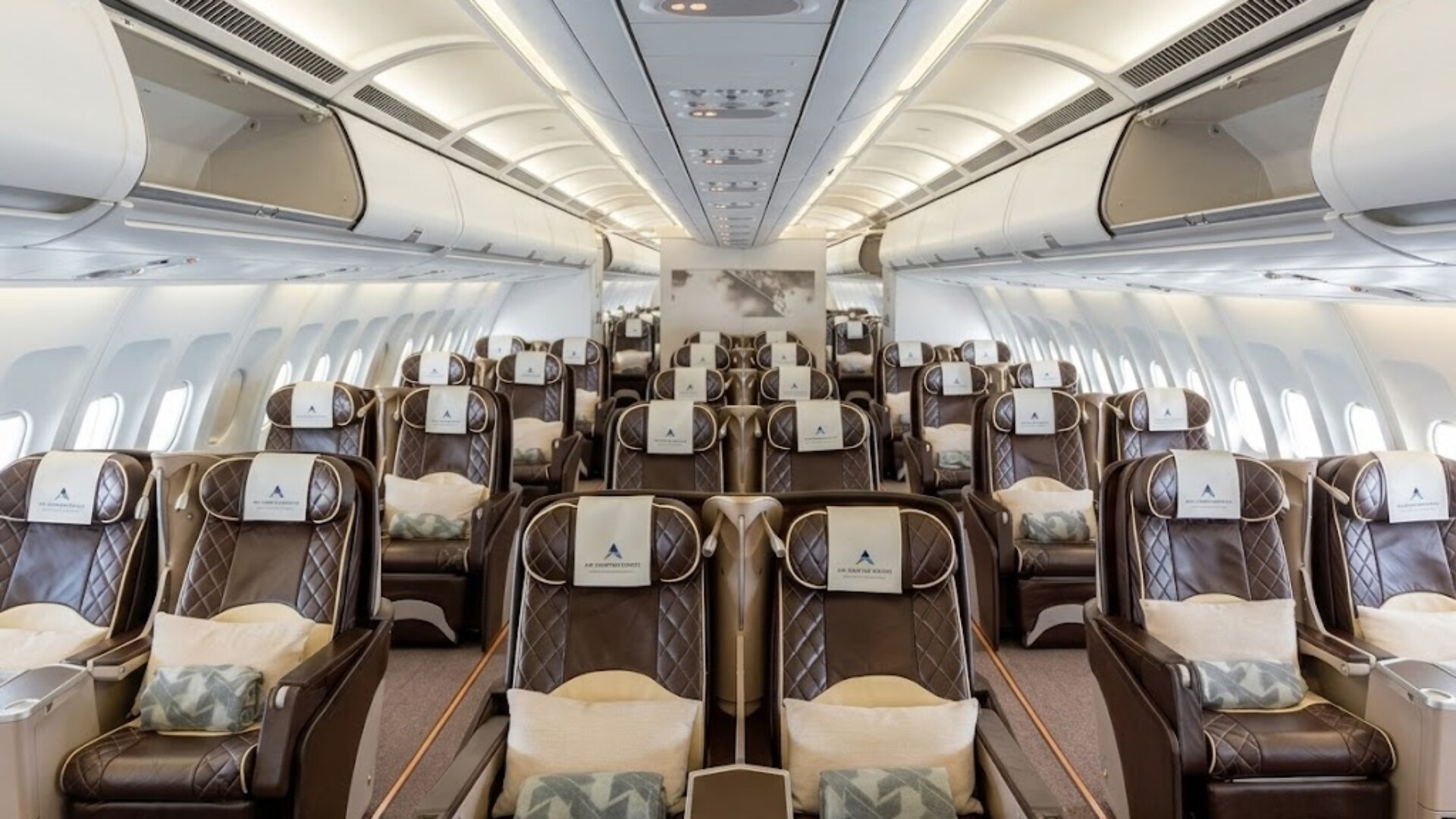 Interior of a modern airplane cabin with many brown leather seats and overhead bins.