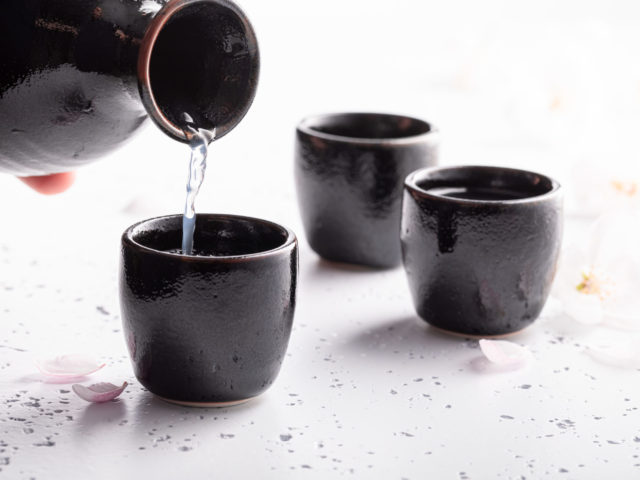 Japanese sake with blooming cherry. Traditionally served sake in ceramics. Black ceramics on a white stone.