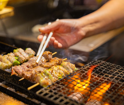 Cropped hand of vendor preparing meat. Man is making food on barbecue grill. He is holding chopsticks.